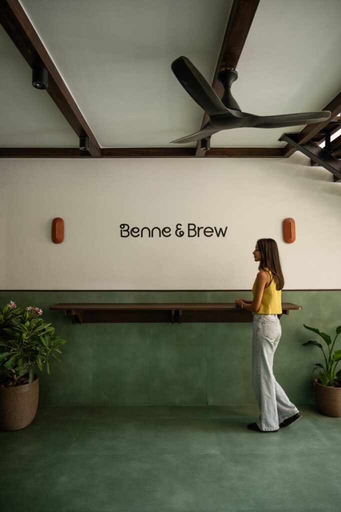 A guest standing at the counter ledge inside Benne & Brew, below the Benne & Brew lettering on the cream wall above mint-green wainscoting