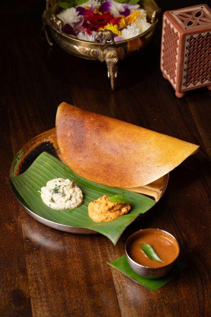 A golden benne masala dosa on a banana leaf with coconut chutney, red chutney and sambar