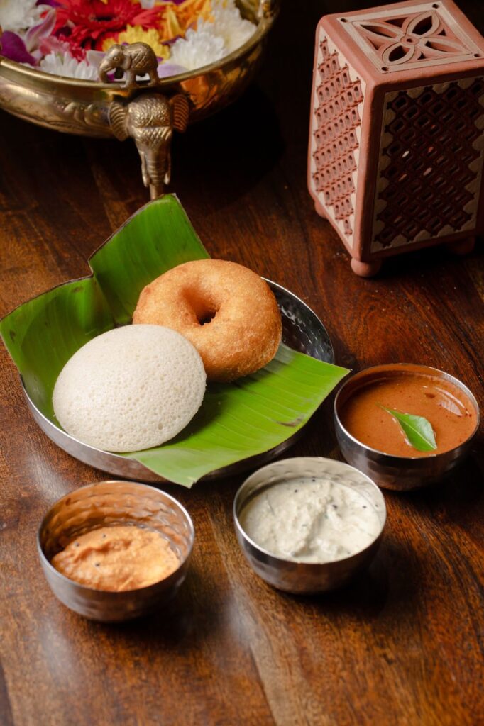 An idli and a medu vada together on a banana leaf