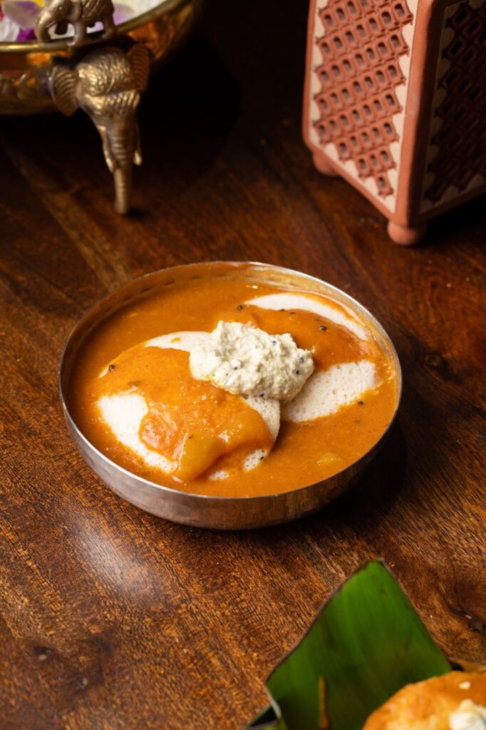 Idli soaking in sambar topped with coconut chutney