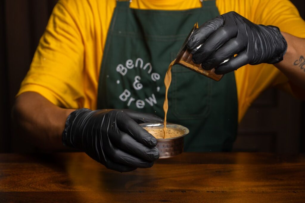 A barista in a Benne & Brew apron pouring filter coffee between a dabara and tumbler