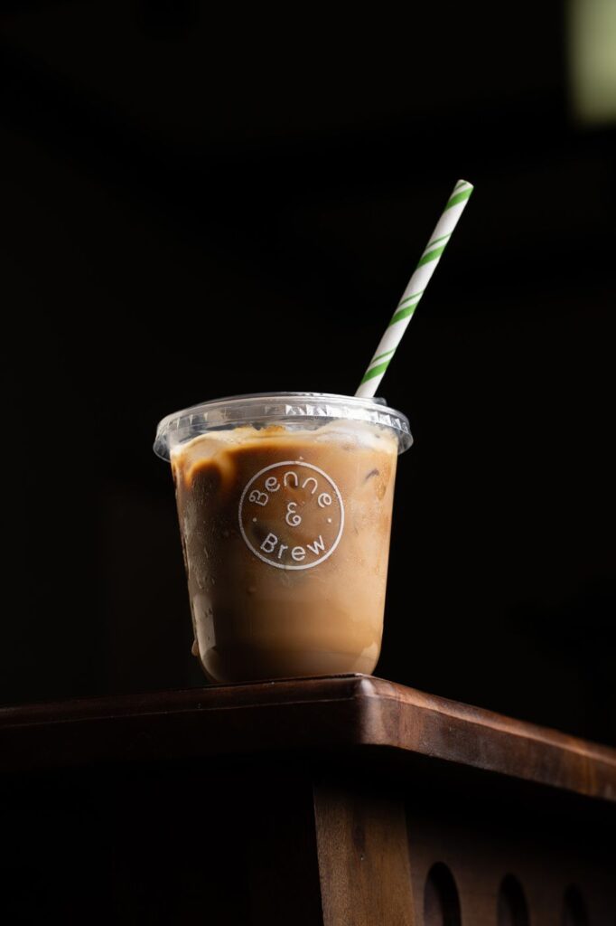 Iced filter coffee in a Benne & Brew cup with a green-striped paper straw
