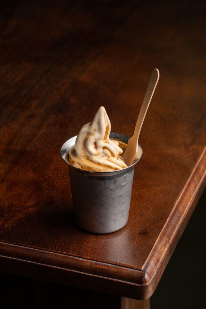 Filter coffee soft serve swirled in a steel tumbler with a wooden spoon