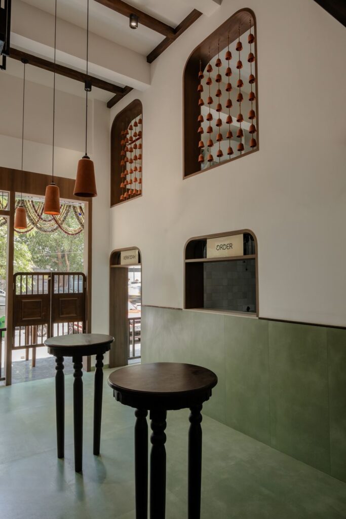 Tall wooden stools by the window at Benne & Brew, under arched niches hung with terracotta bells
